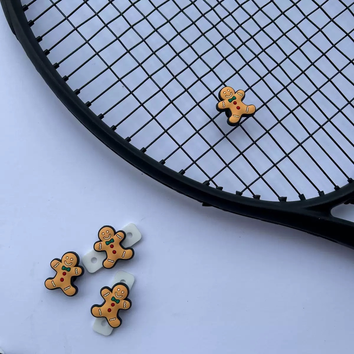 Gingerbread-shaped silicone dampeners shown on and beside a tennis racquet