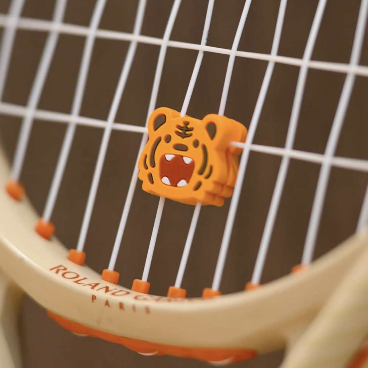 Close view of a tiger-shaped silicone dampener between racquet strings