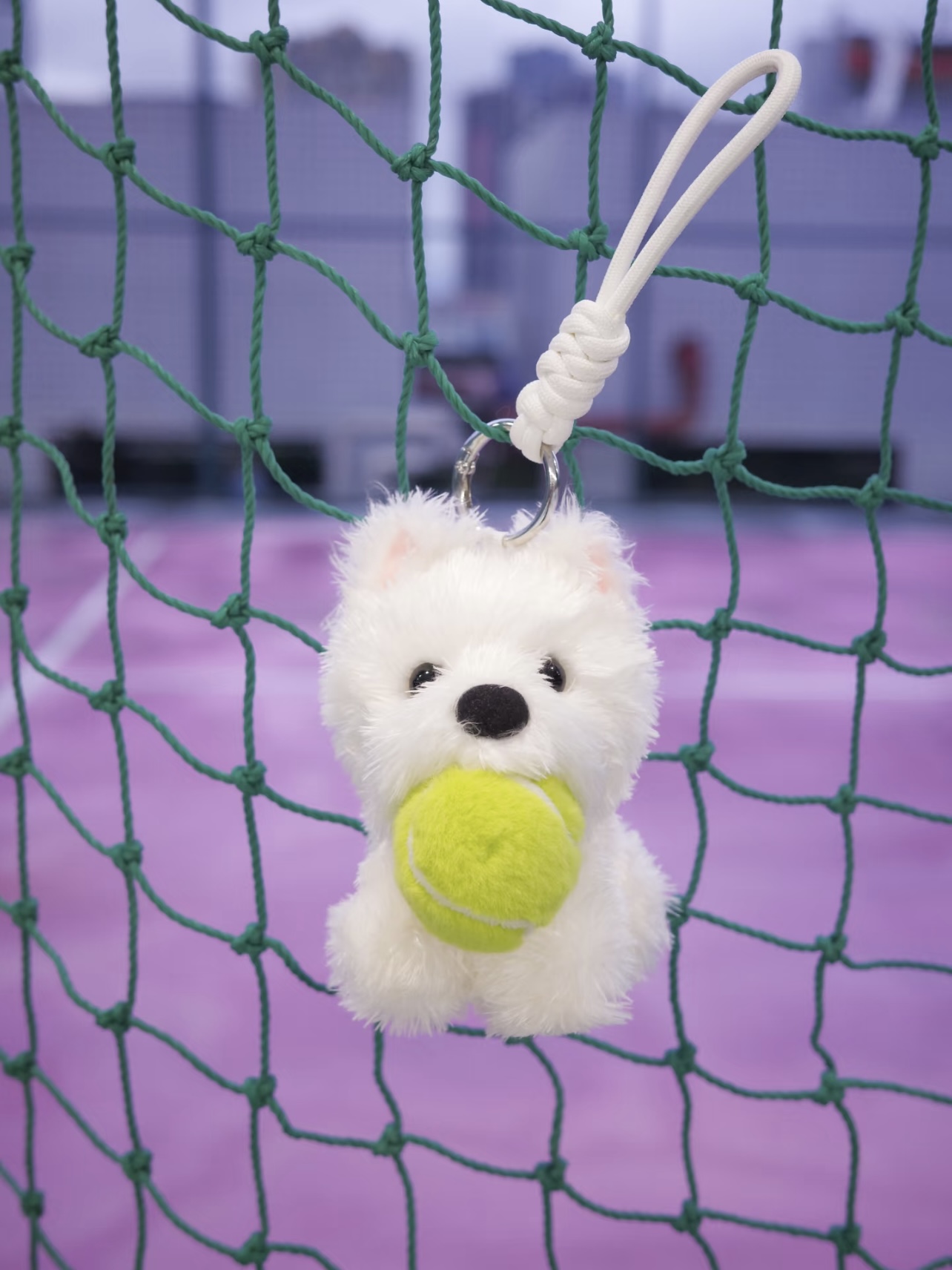 White tennis-themed plush dog charm displayed on a court net