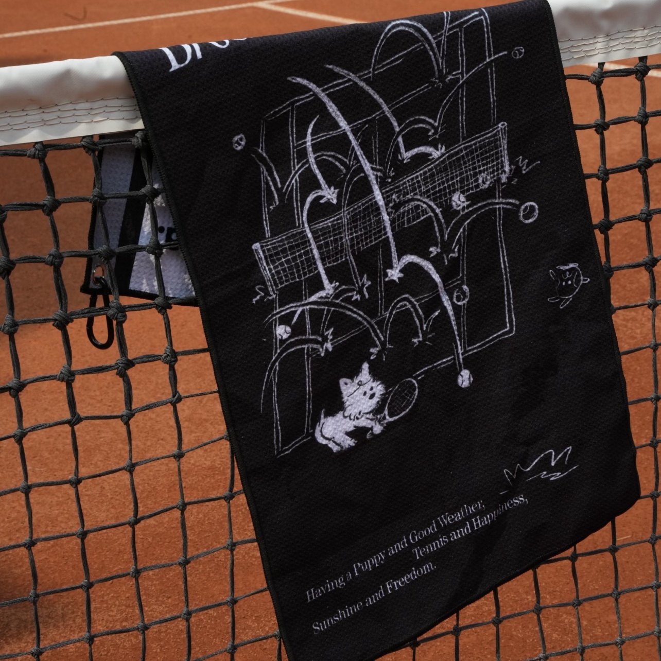 Dark illustrated custom towel hanging from a tennis net