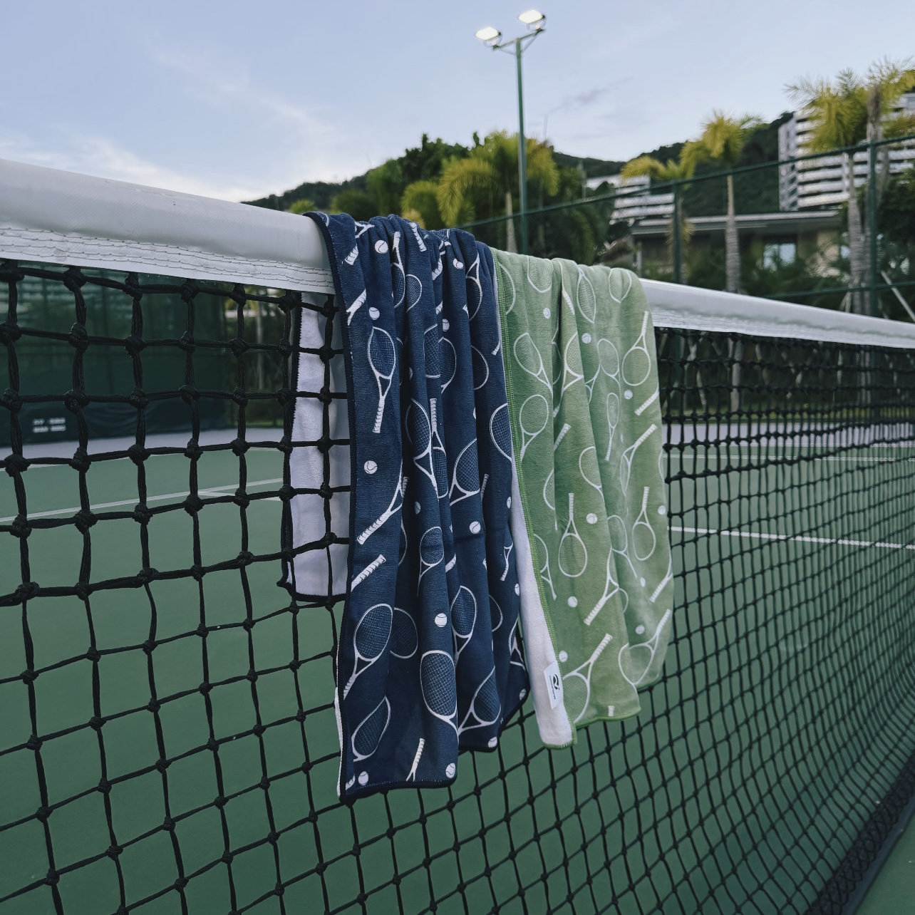 Blue and green custom-pattern tennis towels hanging from a court net