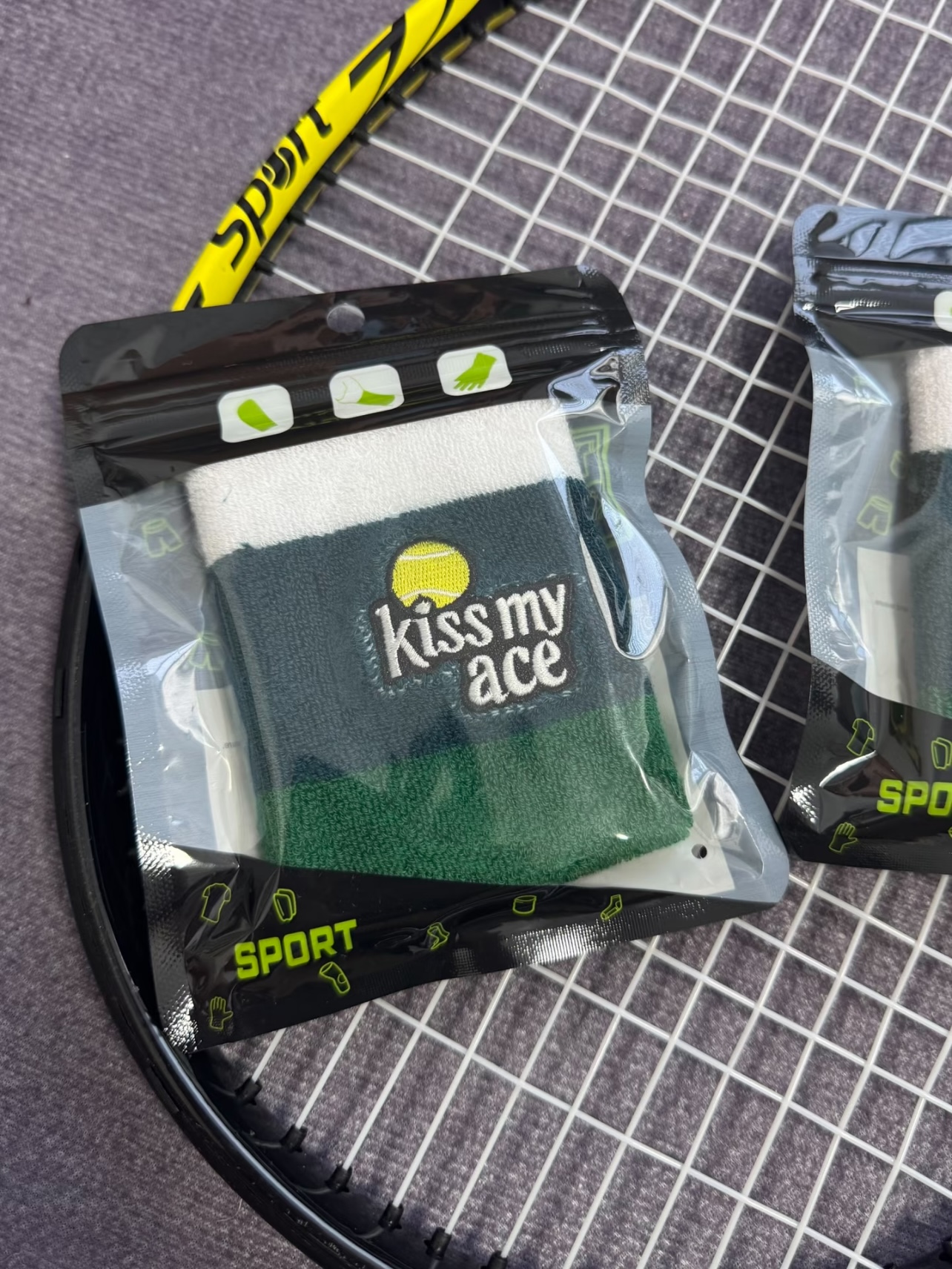 Packaged green wristbands photographed with a tennis racquet